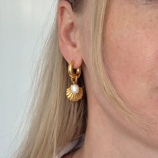 Gold earring with a pearl charm worn by a person with blonde hair.