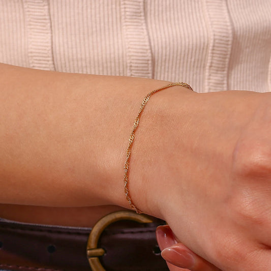 A twisted chain bracelet, made from 18K gold plated stainless steel, on model's wrist