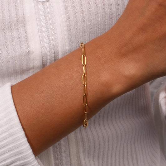 Gold paperclip chain bracelet on a wrist with a neutral background