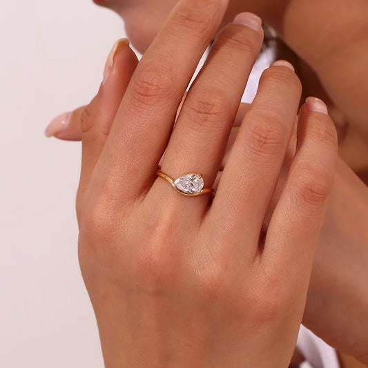 A minimalist gold steel ring with a large drop shaped crystal at its center, set on a simple band.