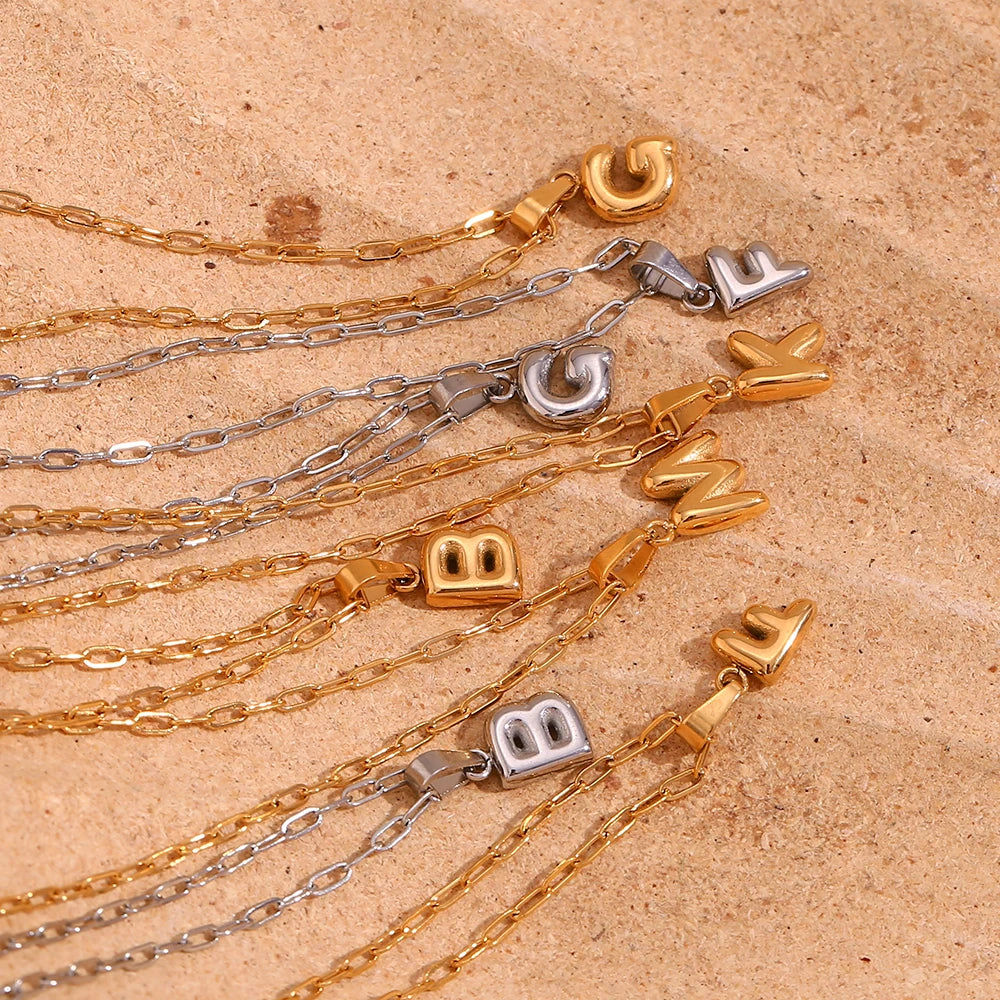 Gold and silver necklaces with letter pendants on a beige surface
