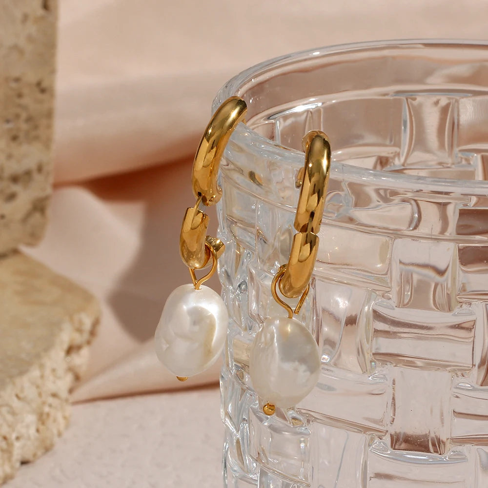 Gold hoop earrings with pearl drops on a clear glass container.
