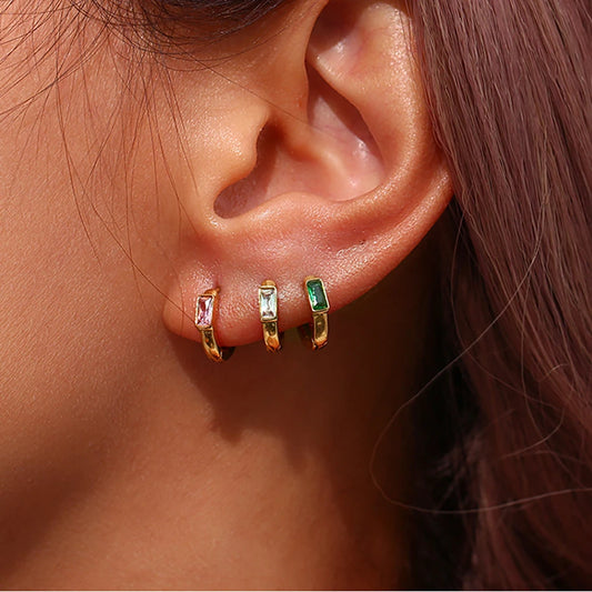 Close-up of an ear wearing gold huggies hoop earrings with gemstones.