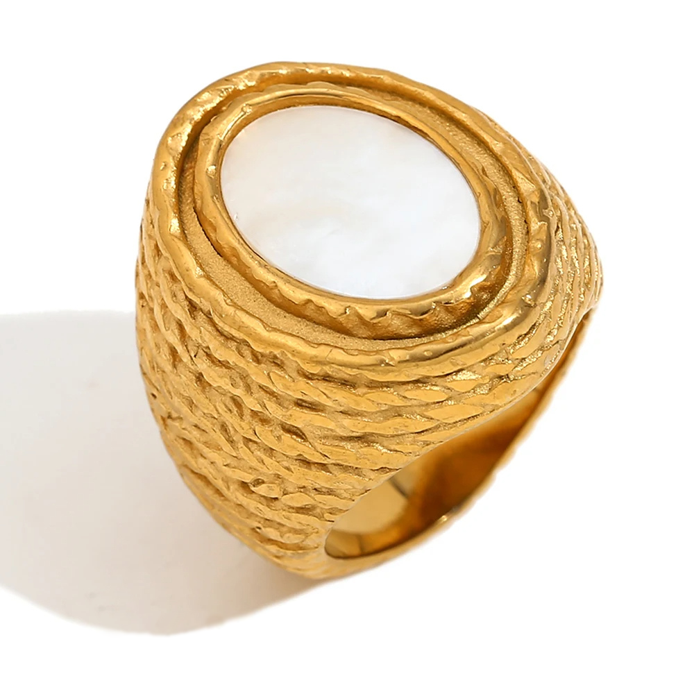 A chunky gold stainless steel ring with a natural white shell inset, set on a white background.