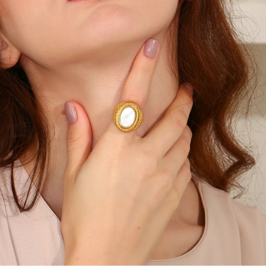 A chunky gold stainless steel ring with a natural white shell inset, on a model's finger