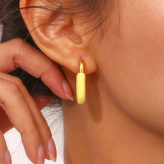 A pair of gold-colored hoop earrings with a pastel yellow coating on model.