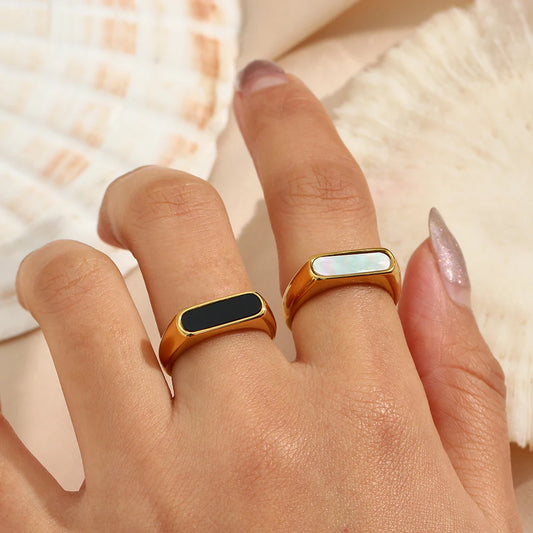 A gold-coated stainless steel rings with a white shell or black acrylic inset, on a model.
