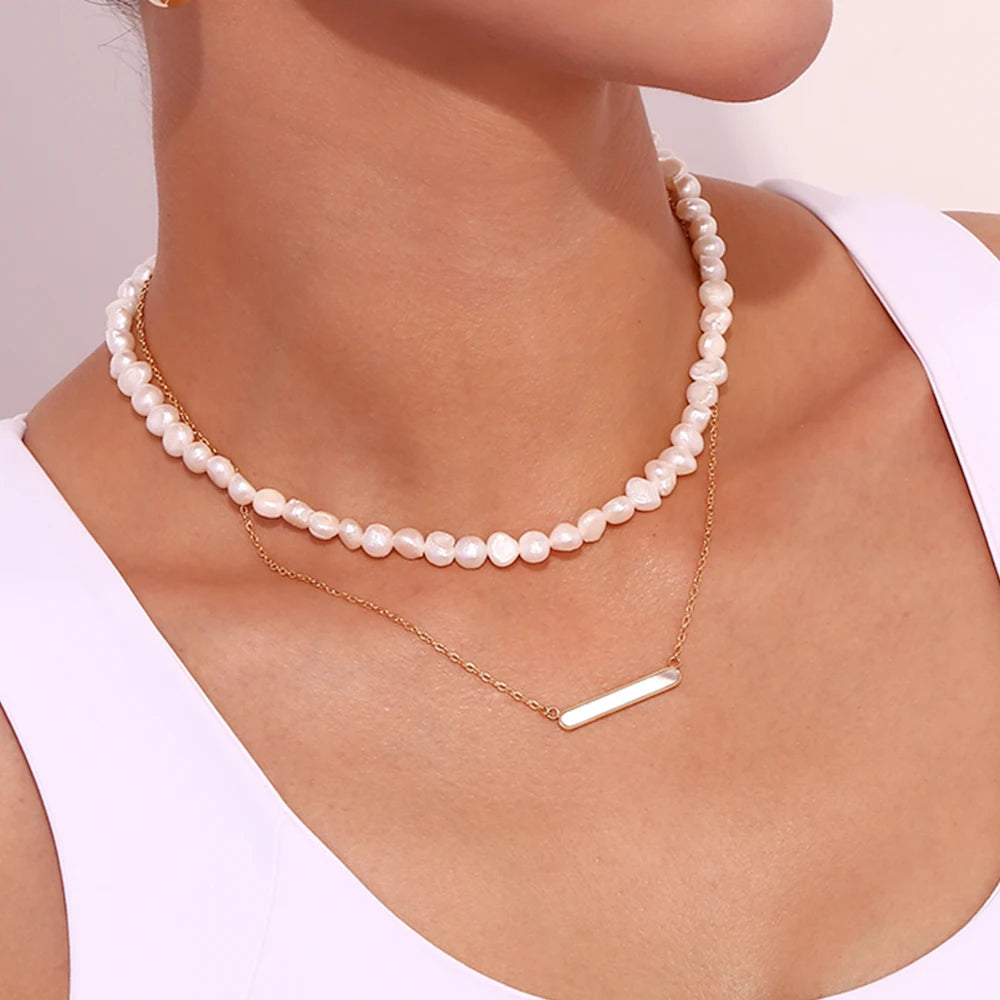 A gold-plated stainless steel necklace with a rounded bar pendant, simple and elegant in design. The necklace is displayed on a model, combined with a pearl necklace.