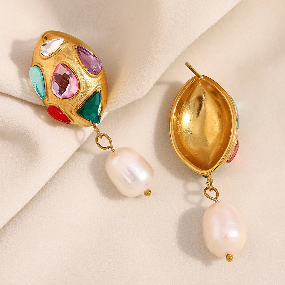 Gold earrings with colorful gemstones and pearl drops on a beige fabric background