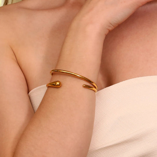 A gold steel bangle bracelet with a sleek, minimalist design, displayed on model's wrist