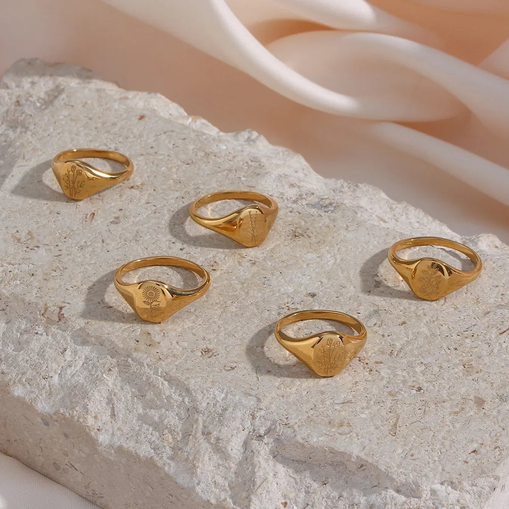 Set of gold steel signet rings on a textured stone surface with a soft peach background