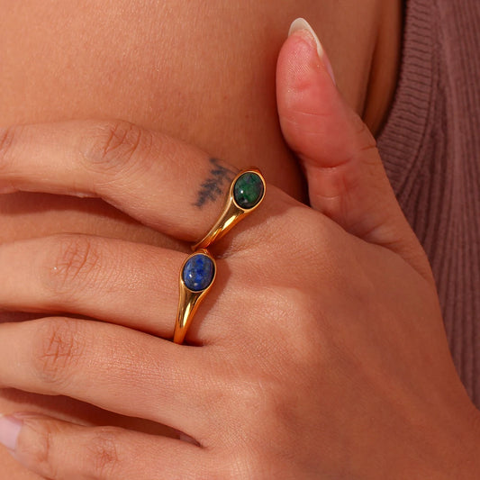 Golden rings with oval blue or green gemstones set in the center, displayed on model