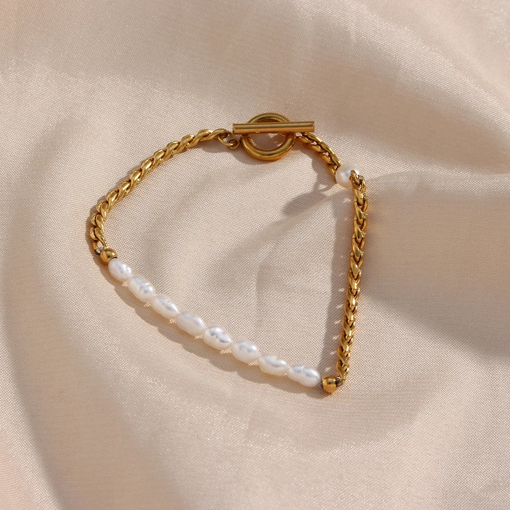 A gold bracelet with twisted chain design and pearl accents, displayed on a beige fabric surface.