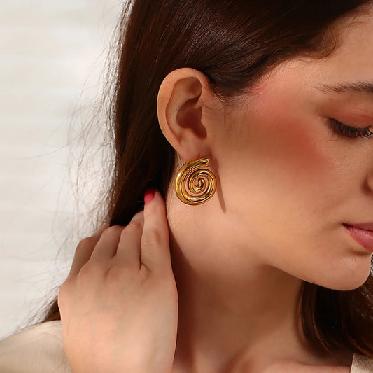 A pair of 18K gold plated stainless steel earrings with a spiral design on a model