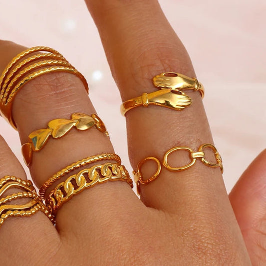 An adjustable gold ring with a minimalist linked design combined with other rings on model.