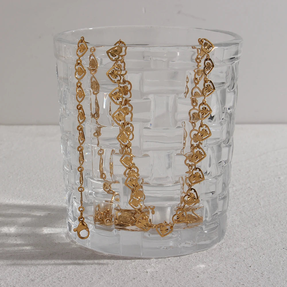 A gold bracelet with heart-shaped links and a natural pearl featured towards the end.