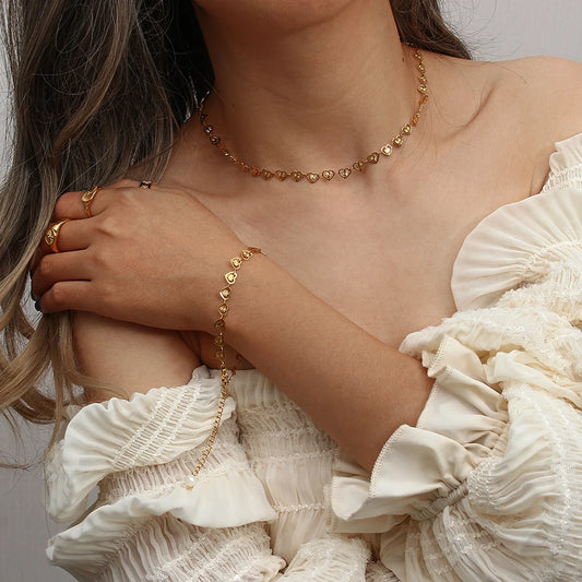 A gold bracelet and necklace with heart-shaped links and a natural pearl featured towards the end on a model