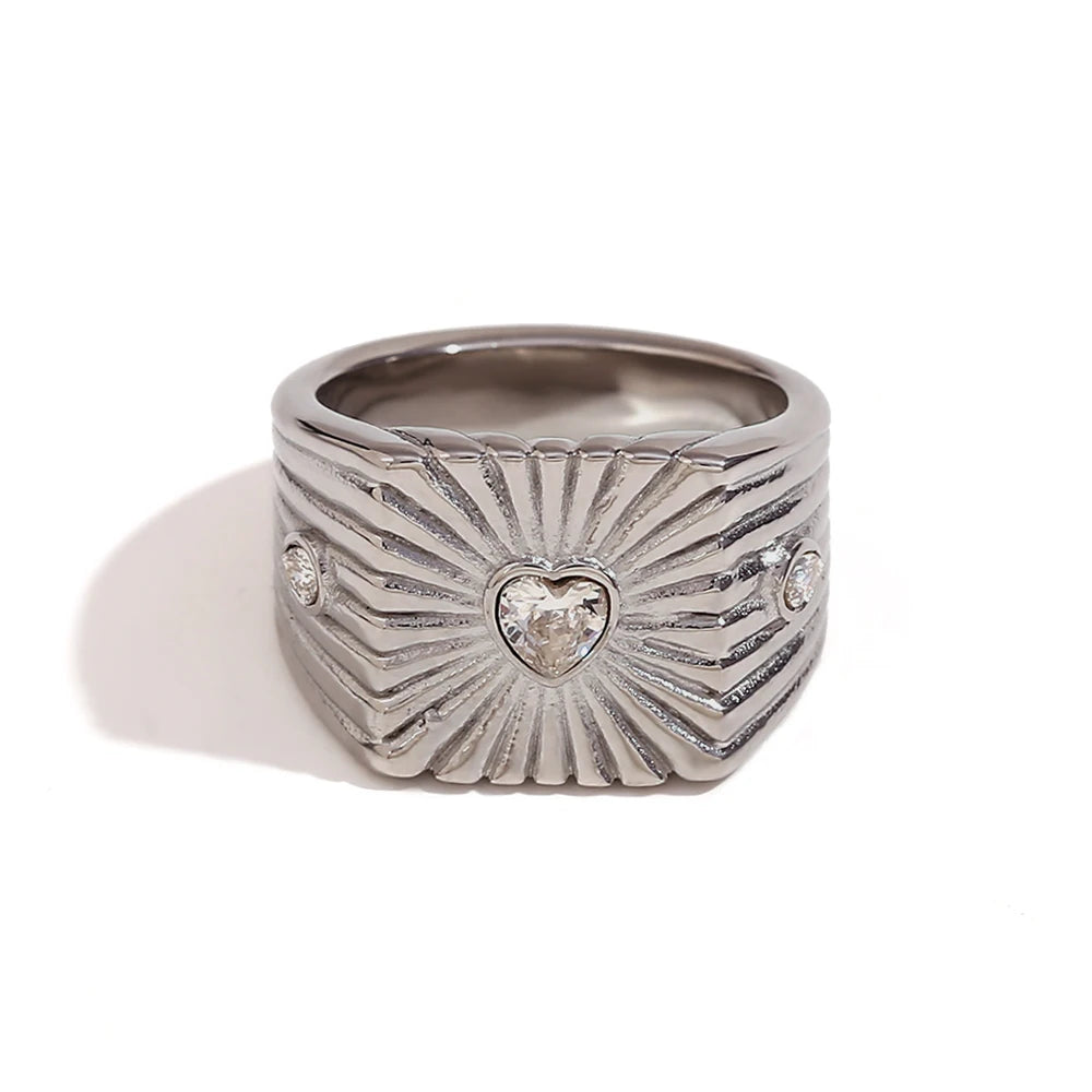A stainless steel signet ring with a geometric design and crystal accents, featuring a prominent heart shaped zirconia at the top.