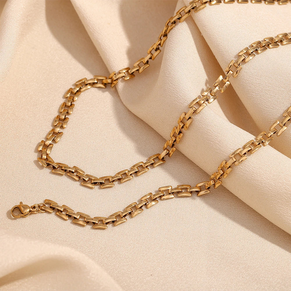 A gold-plated stainless steel necklace with a box chain design, displayed against a fabric background