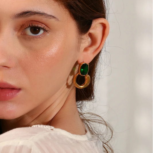A pair of gold-colored earrings with deep green or black oval stones set in a loop design on model