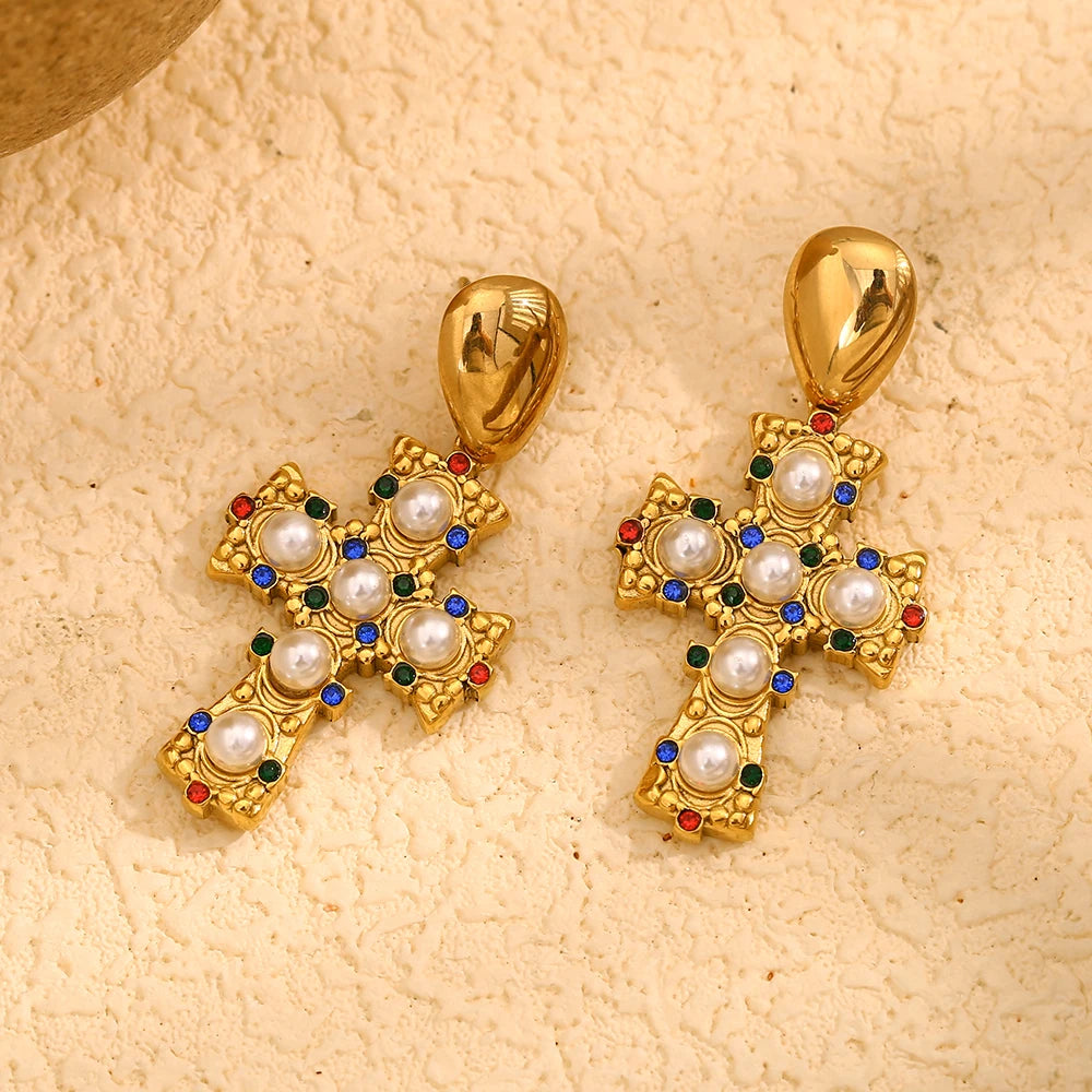 A pair of gold-plated earrings in the shape of a cross, adorned with multicolored zirconia and pearls flat lay