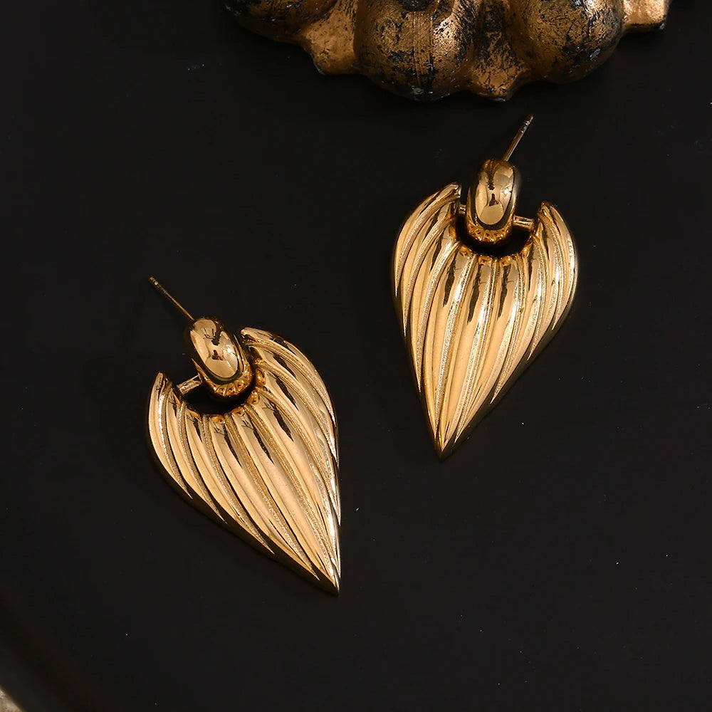 A pair of golden point earrings with a textured design, attached to a black background.