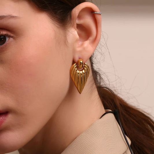 A pair of gold pointed earrings with a textured design, shown in a model's ear