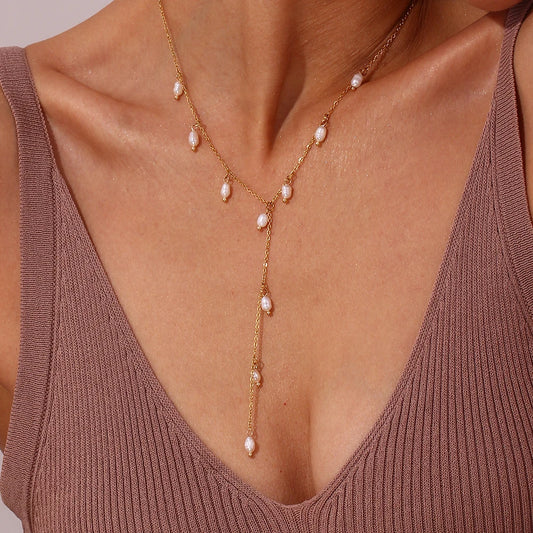 A gold lariat necklace with natural pearls, featuring a delicate design with multiple pearl drops along the chain on a model