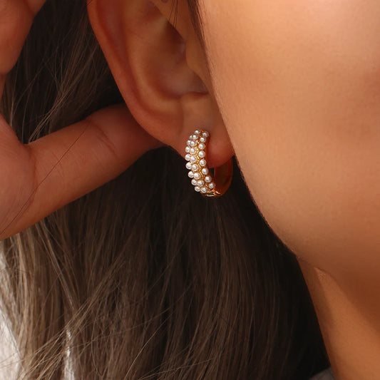 Close-up of a person wearing a gold hoop earring with pearls.