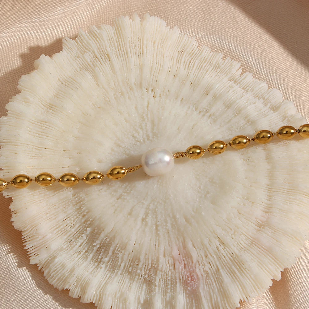 A gold stainless steel beaded necklace with a natural pearl at its center