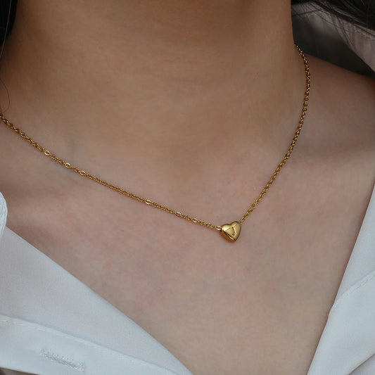 Gold necklace with a heart initial letter pendant on a person wearing a white top.