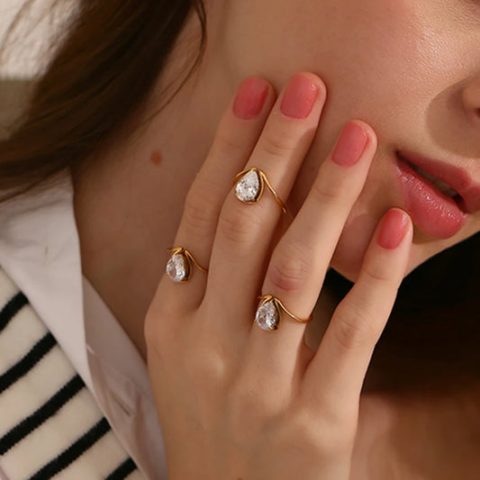 A gold stainless steel ring with a large teardrop-shaped clear zirconia centerpiece.