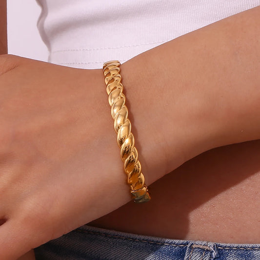 A gold twisted bangle bracelet with a shiny finish on a models wrist