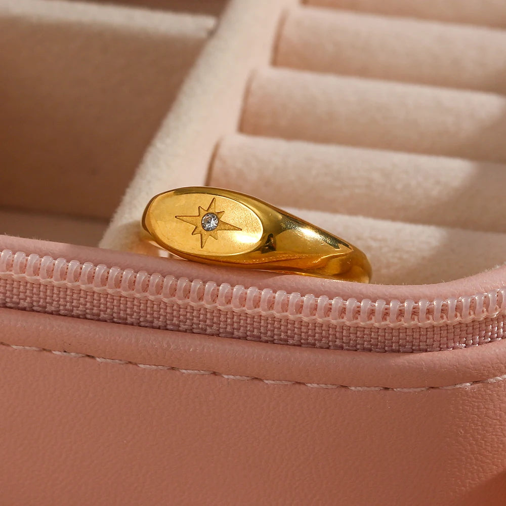 A stainless steel signet ring with a crystal embellishment, displayed on a pink jewelry box.