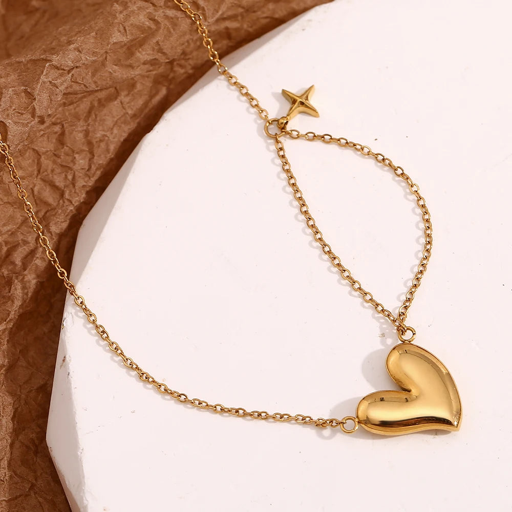 A gold steel necklace with a heart-shaped pendant and a small star charm