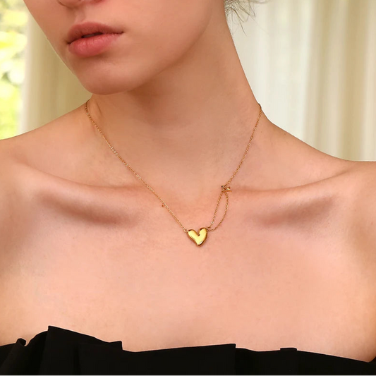 A gold steel necklace with a heart-shaped pendant and a small star charm on a model