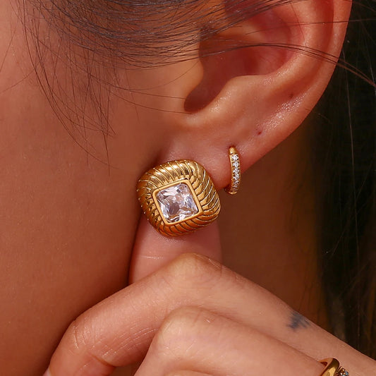 A pair of stainless steel stud earrings with a geometric design and a central clear crystal in a woman's ear.