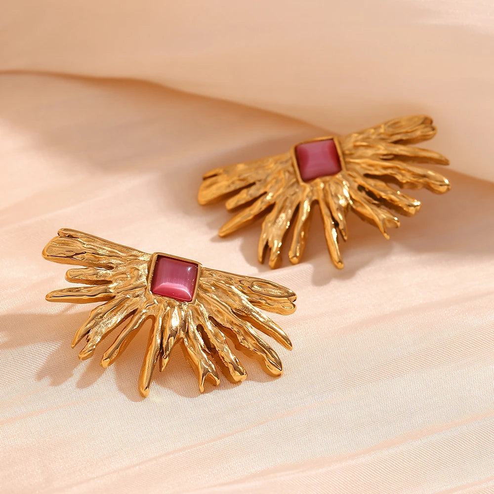 A pair of gold-colored earrings designed to resemble sun rays with a square pink gem at the top.