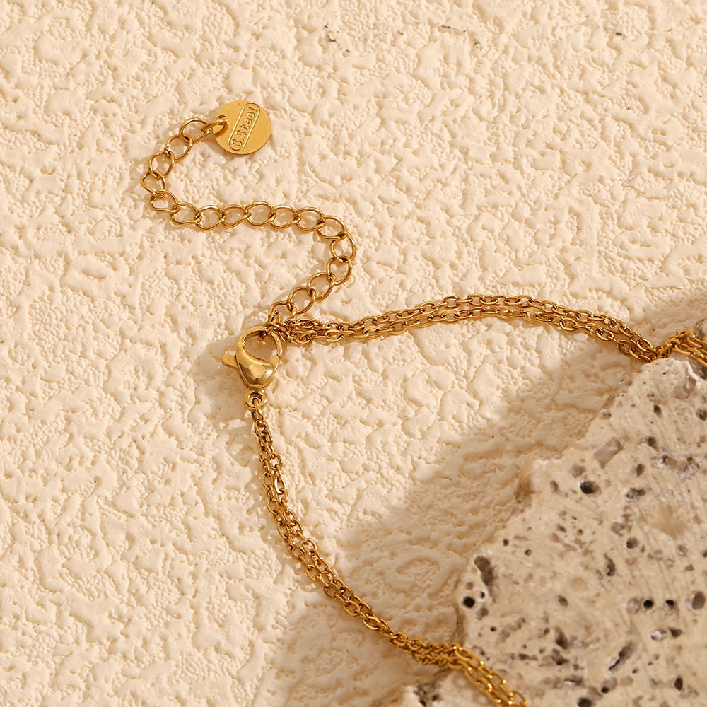 A double layered necklace with gold chains and heart-shaped pendants, one of which is made from a natural shell