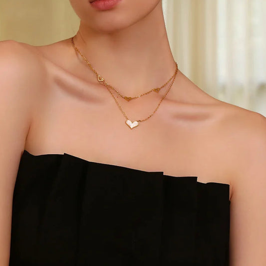 A double layered necklace with gold chains and heart-shaped pendants, one of which is made from a natural shell, displayed on a model