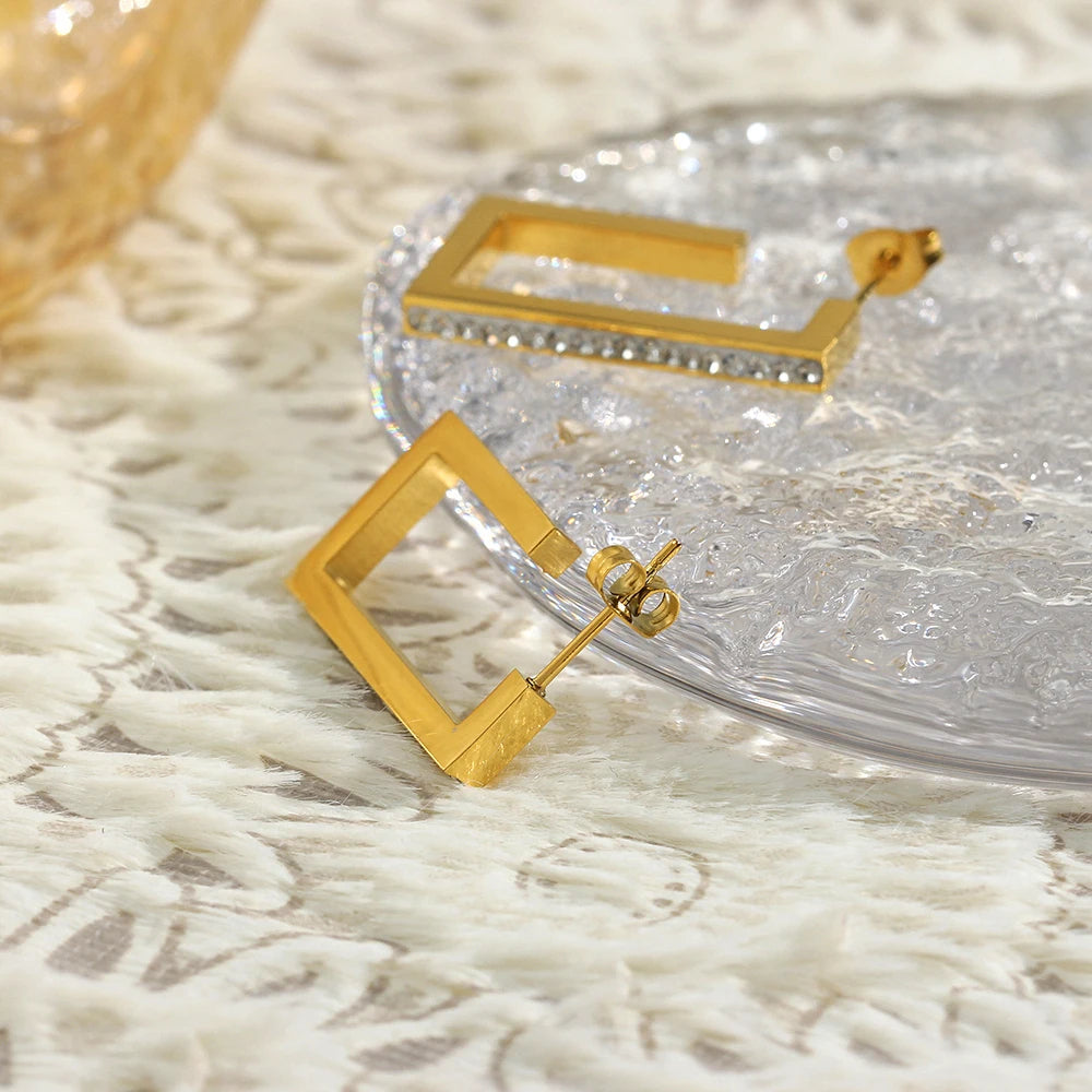 Gold square hoop earrings on a textured surface