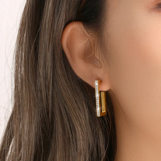 Rectangular earring worn by a person with dark hair on a neutral background