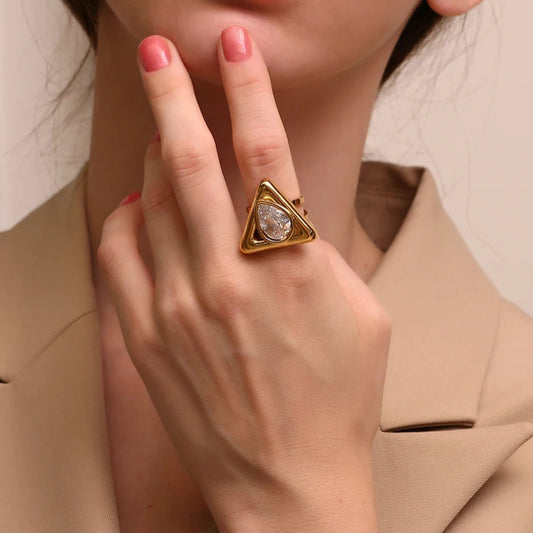 An gold stainless steel ring with a triangular design and a large, clear zirconia centerpiece.