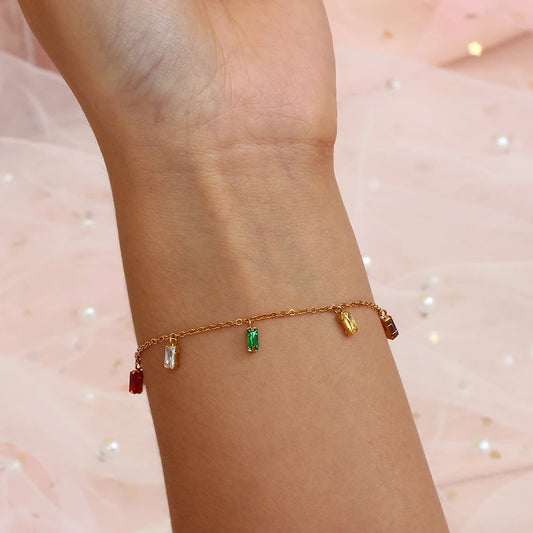 A golden bracelet with multicolored zirconia charms on a model's wrist