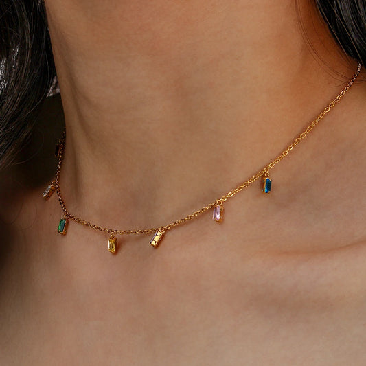 A golden necklace with multicolored zirconia charms attached to a gold chain, on a model's neck