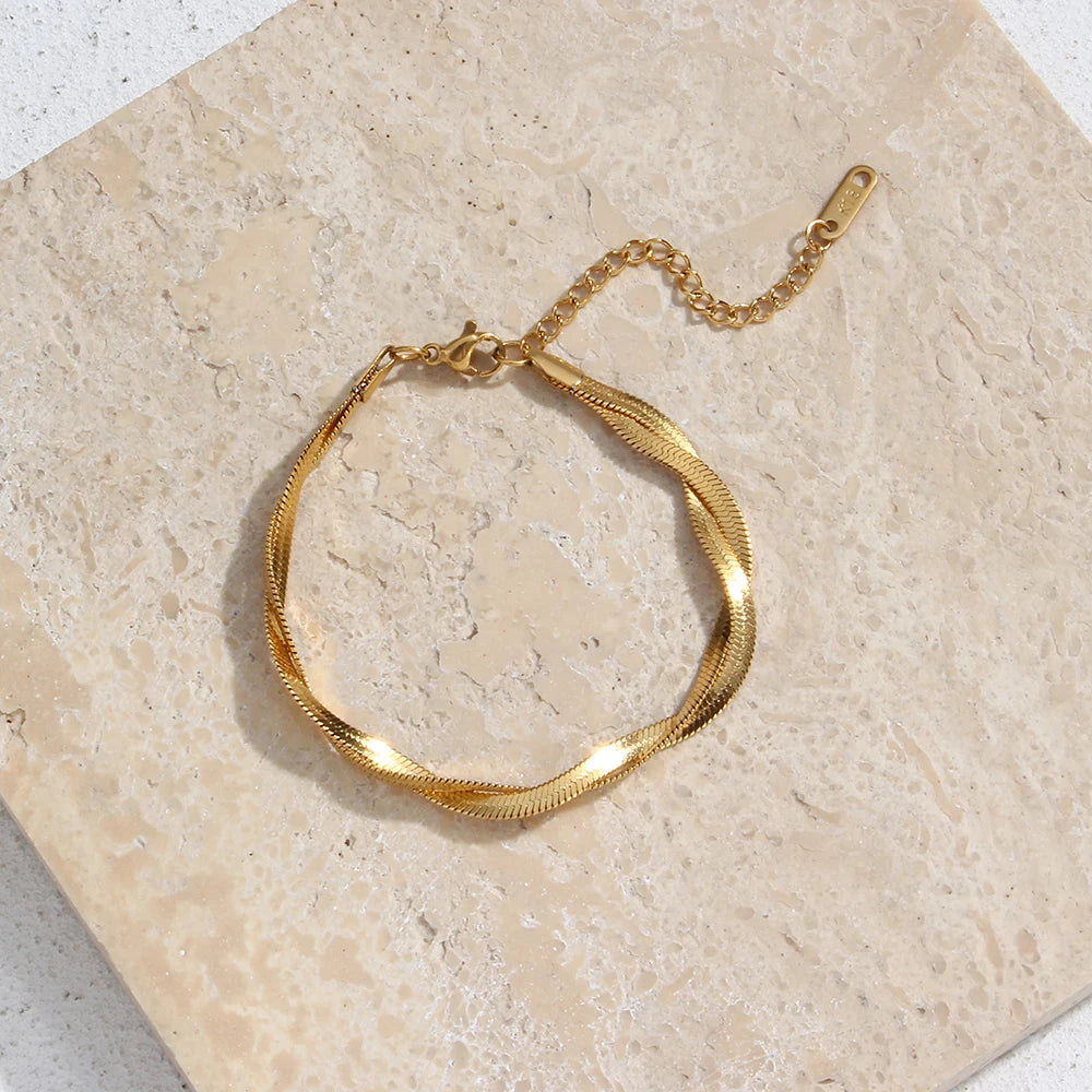 A gold twisted snake chain bracelet flat layed on a textured background.