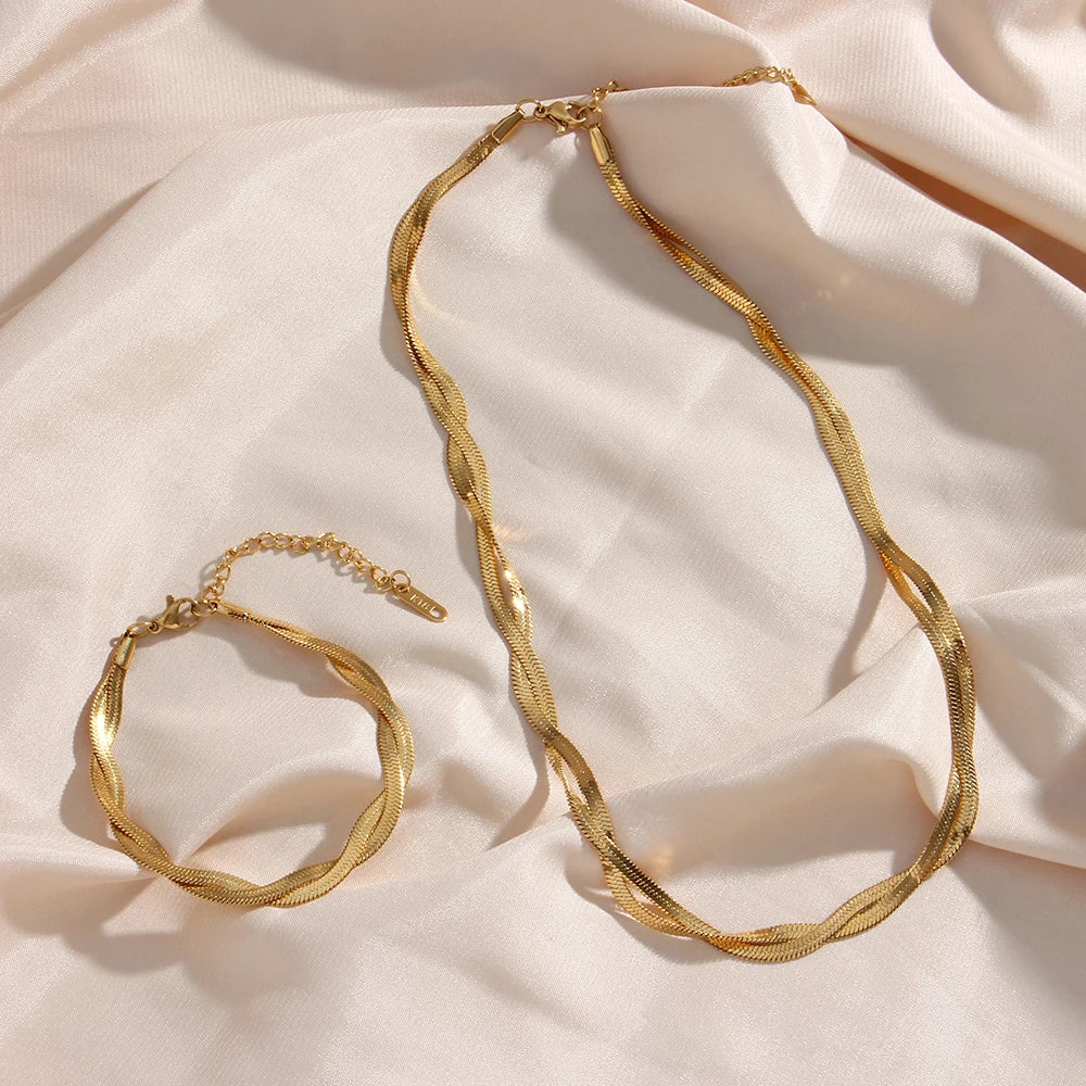 A gold twisted snake chain Necklace and bracelet made from 18K gold plated stainless steel, flat layed on a fabric background.