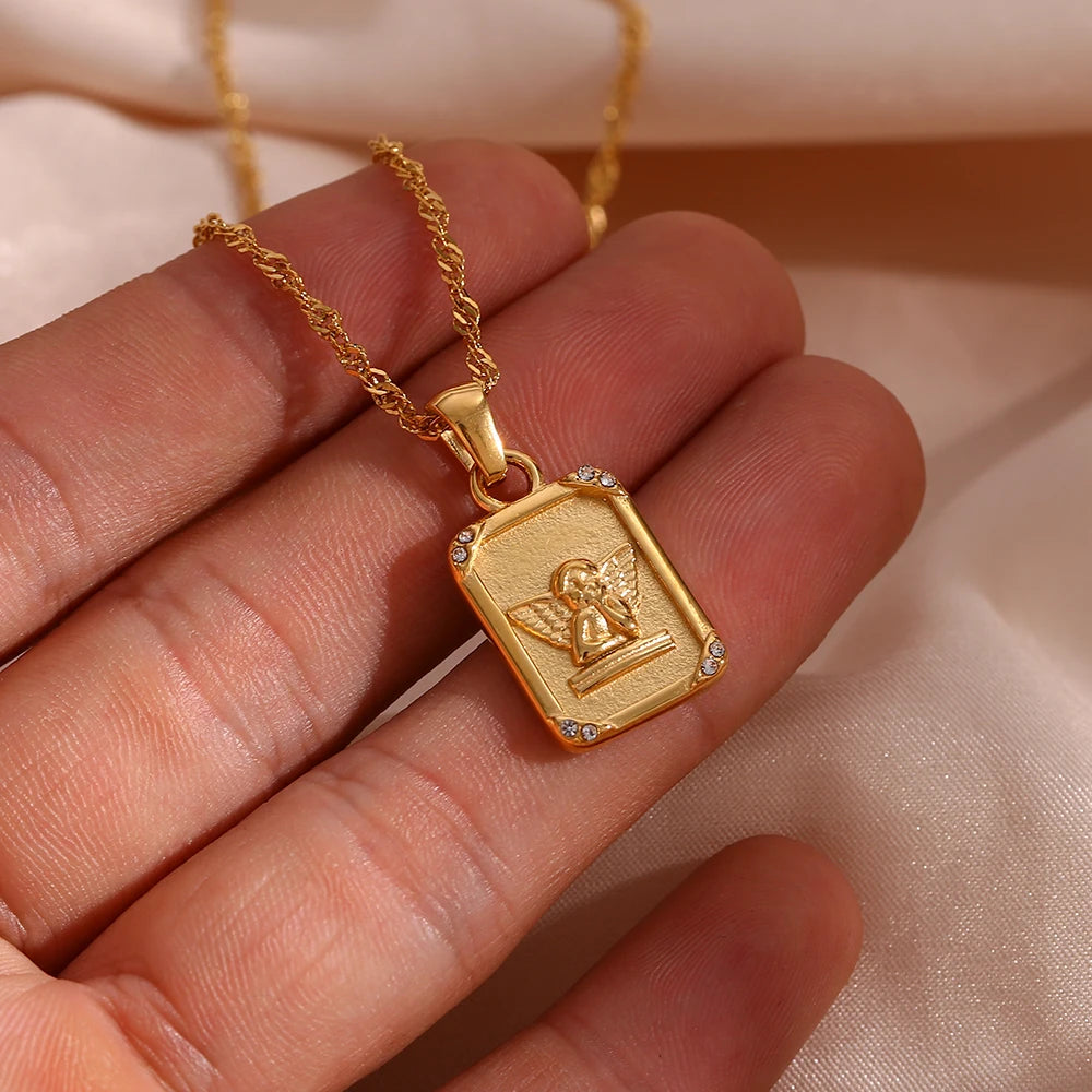 A gold-plated stainless steel necklace with a square pendant featuring an angel figure, displayed on a human hand
