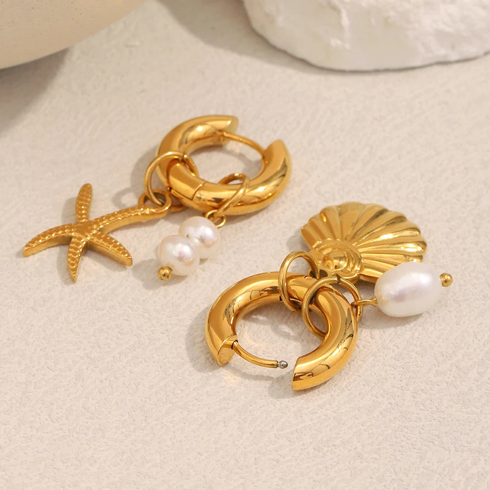 Gold hoop earrings with starfish, shell, and pearl charms on a beige surface.
