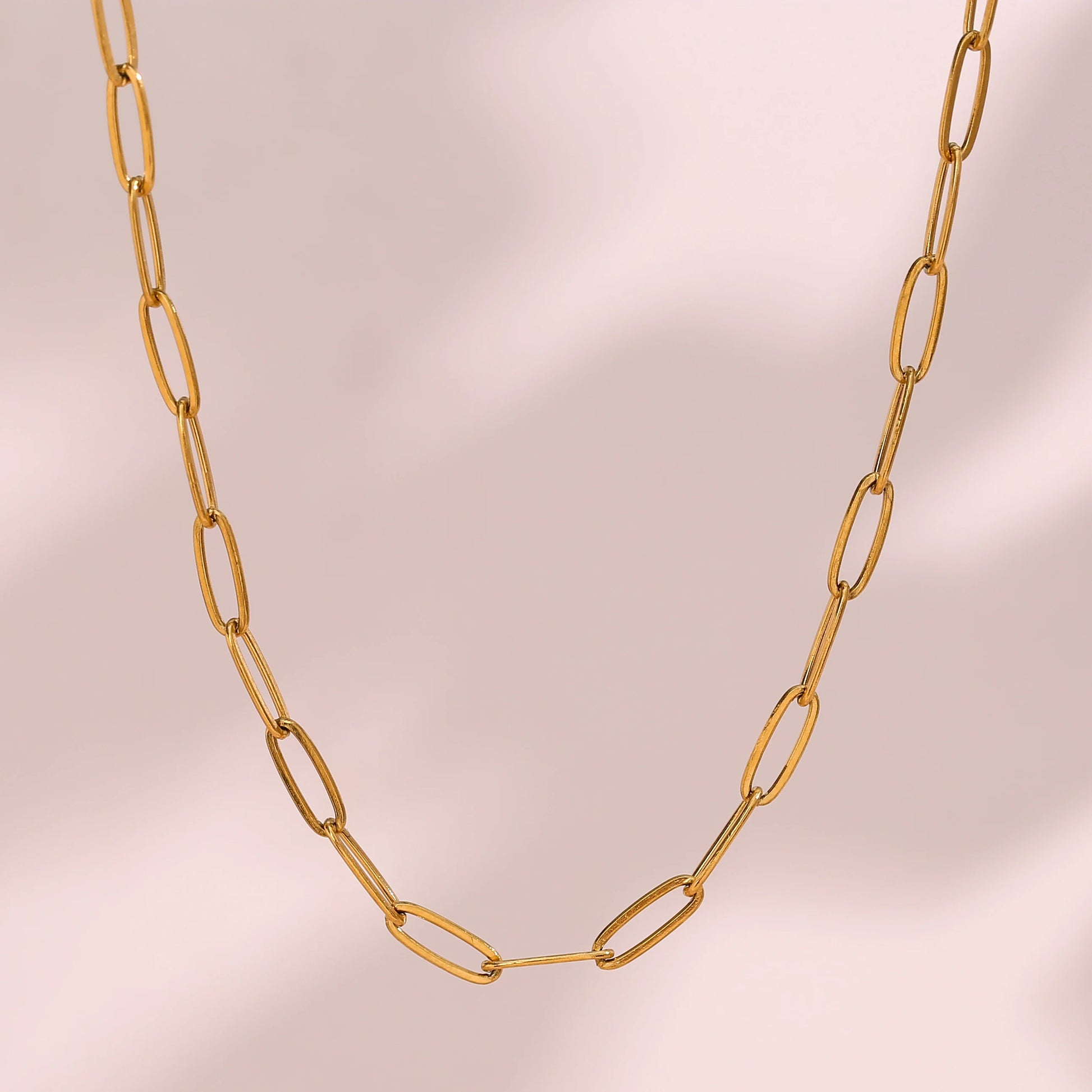 Gold paperclip necklace on a beige background